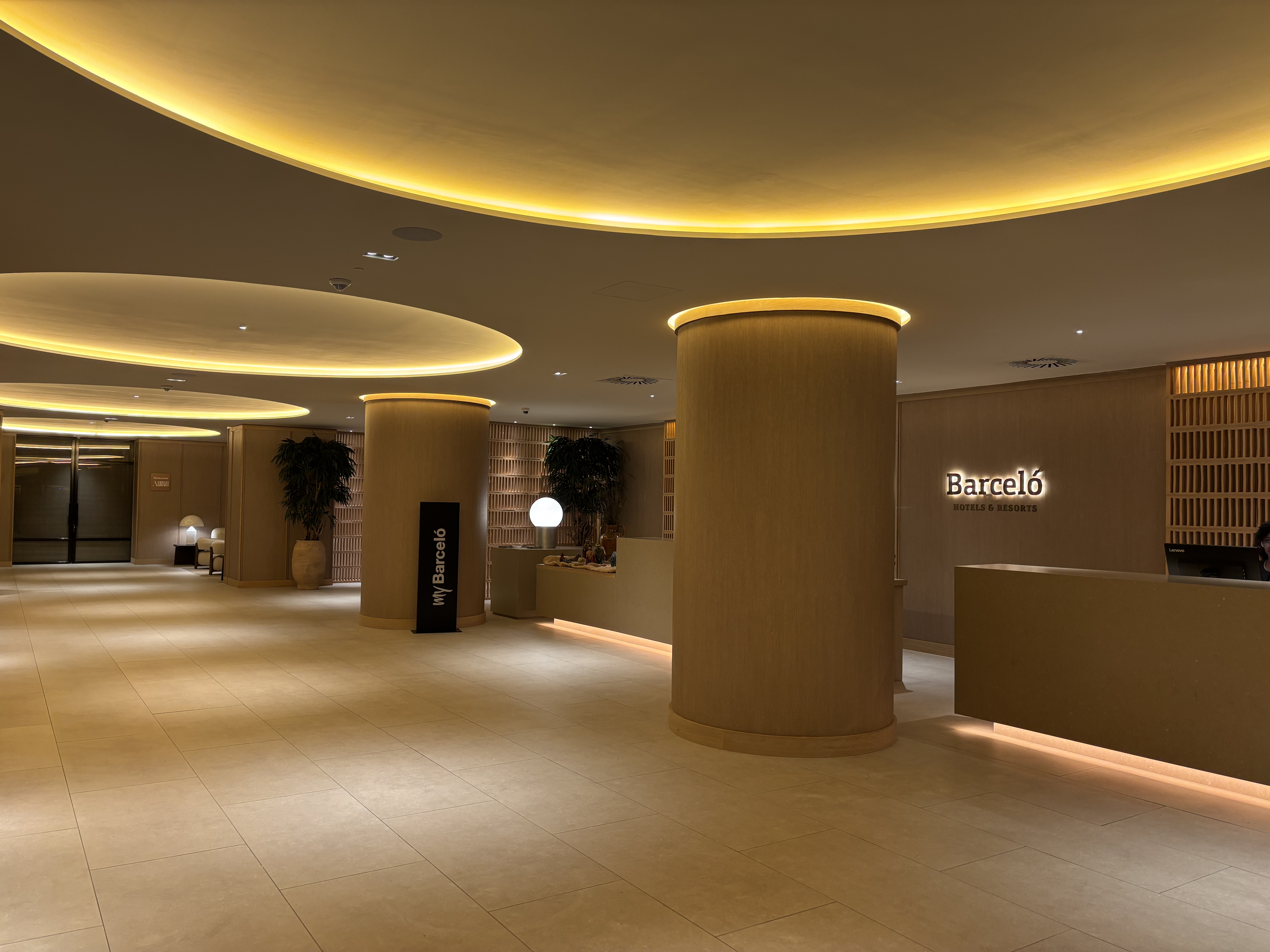 L'image montre l'intérieur d'un hôtel moderne, probablement un hall ou une réception. L'espace est vaste, avec un design minimaliste et élégant. ...