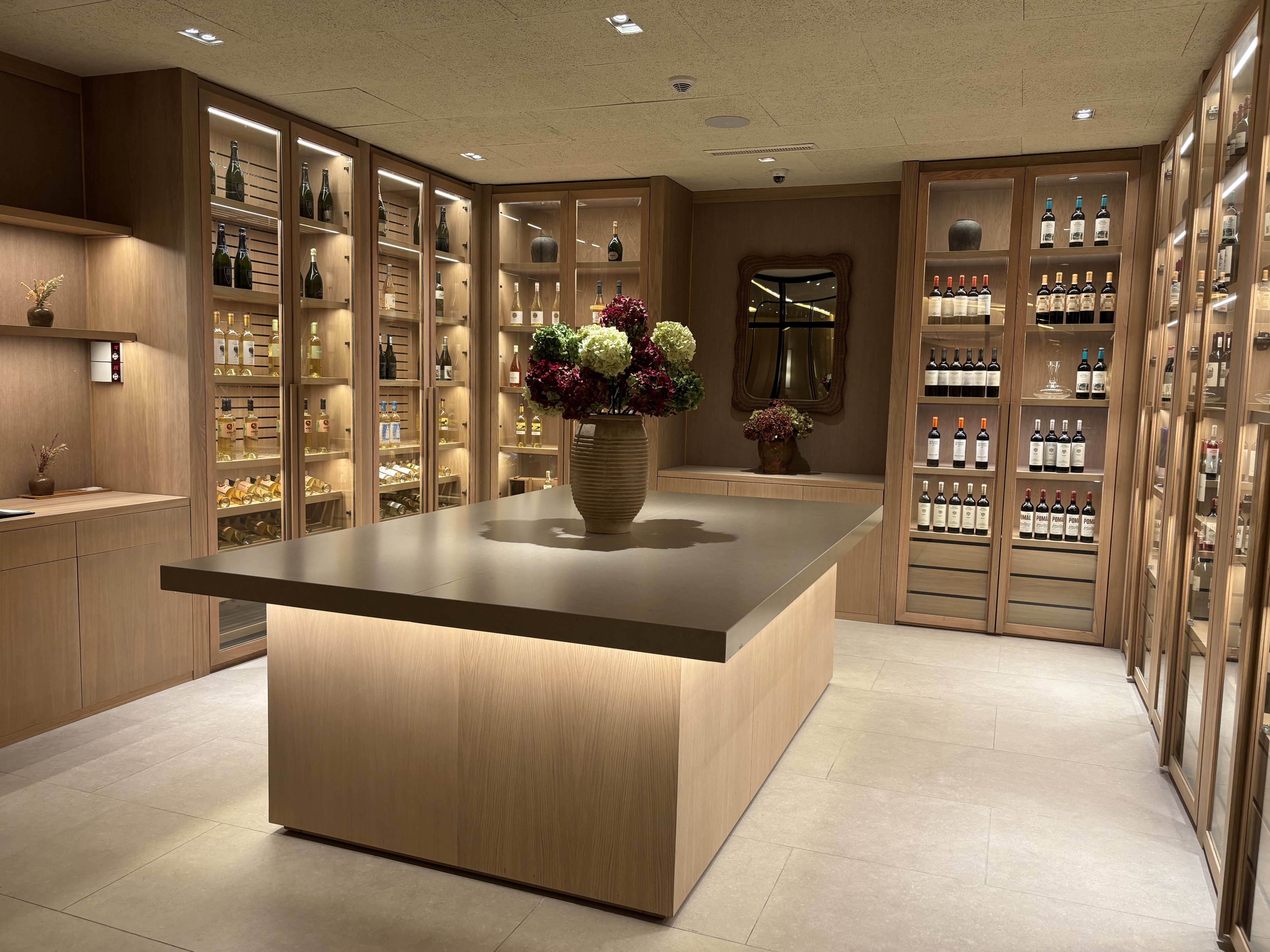 L'image montre la cave à vin du restaurant. Elle est composée d'étagères en bois clair contenant diverses bouteilles de vin, de champagne et de ...