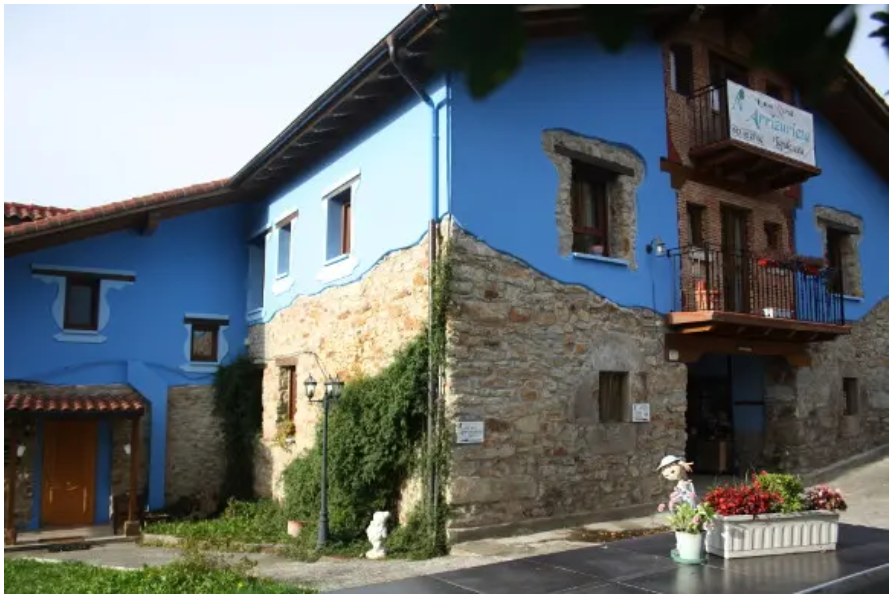 Vue extérieure d’une maison rurale traditionnelle associant des murs en pierre naturelle et des façades peintes en bleu vif. Le bâtiment dispose ...