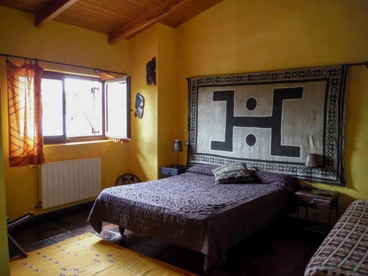 L’image montre une chambre de style ethnique avec des murs jaunes, un plafond à poutres en bois et un sol foncé. Au centre, un lit double avec une ...