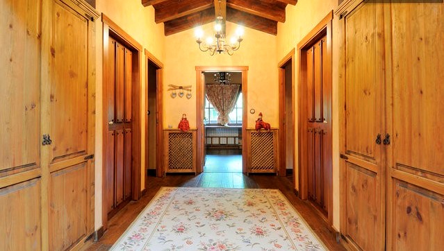 This photograph shows the hallway of a home with a rustic design, dominated by wooden elements including the floor, the doors of the side closets, ...