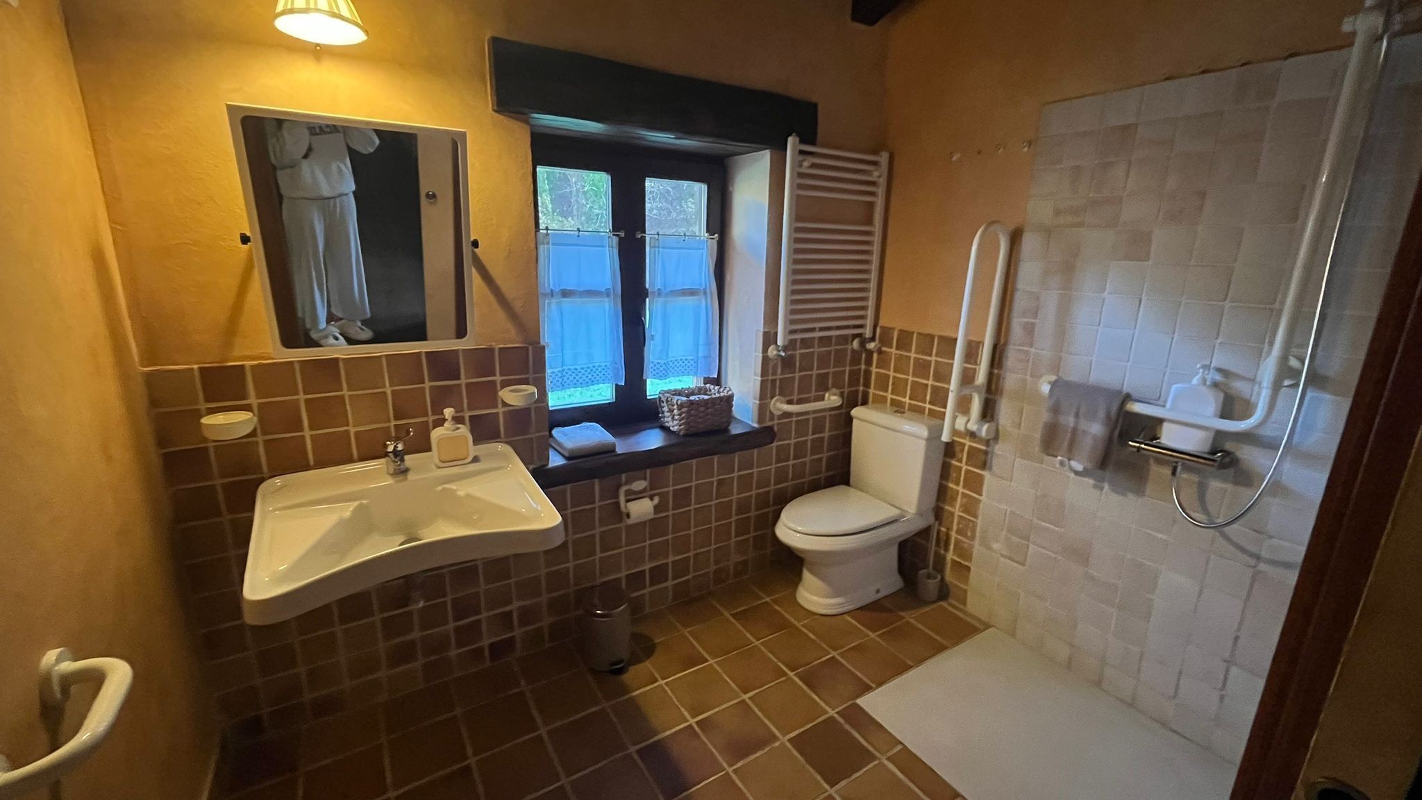 Accessible bathroom with generous circulation space. It features a wall-mounted sink, a toilet with foldable grab bars, and a walk-in shower with ...